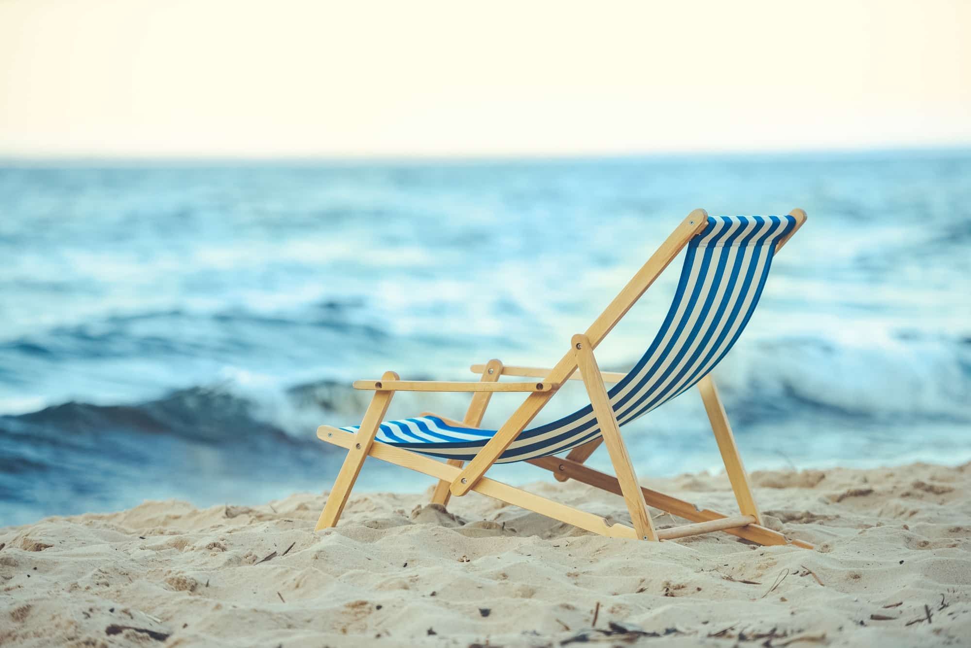 selective focus of wooden beach chair on sandy beach with sea on background